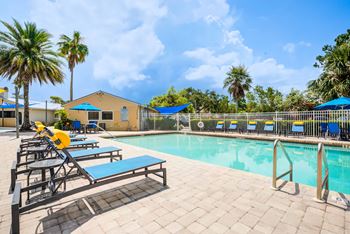 A pool area with sun loungers and a yellow building in the background